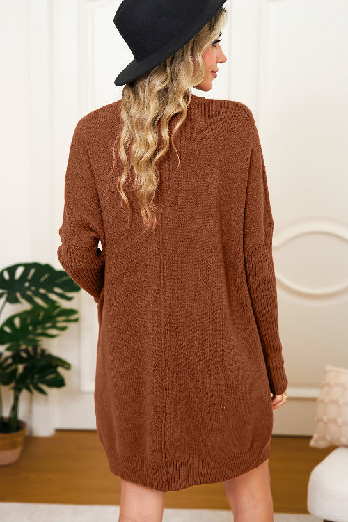 Woman wearing a brown sweater dress and black hat in a room with a plant and decorative wall.