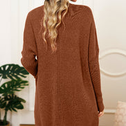 Woman wearing a brown sweater dress and black hat in a room with a plant and decorative wall.
