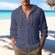 Man wearing a blue button-up shirt with a beach in the background