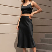 Person wearing a black satin skirt and clear high-heeled shoes on a neutral background