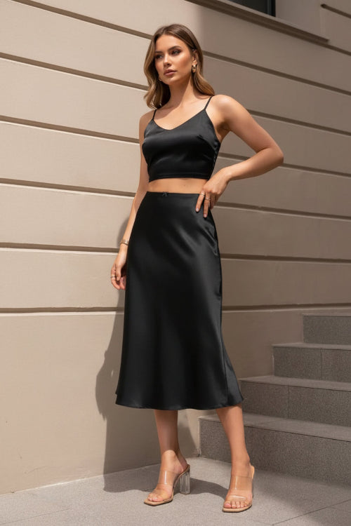 Person wearing a black satin skirt and clear high-heeled shoes on a neutral background