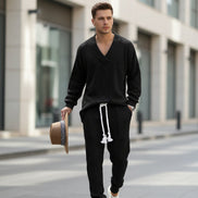 A man modeling a black cable-knit lounge set consisting of a V-neck long-sleeve sweater and matching jogger pants with a white drawstring, 