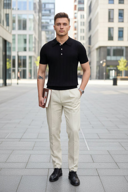 Person wearing a black polo shirt holding a book in a room with a lamp and table.
