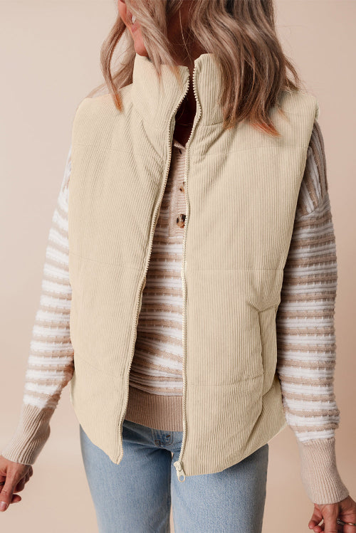 Person wearing a beige quilted vest over a striped sweater with a plain background