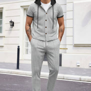 A man wearing a light gray two-piece tracksuit with a short-sleeve button-up hoodie and matching drawstring pants, 