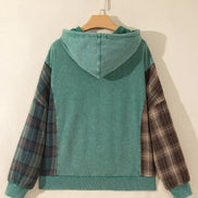 A teal green hooded sweatshirt hanging on a wooden hanger against a plain beige wall, featuring plaid patterned sleeves.