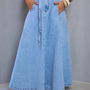 Person wearing a long denim skirt with a plain background