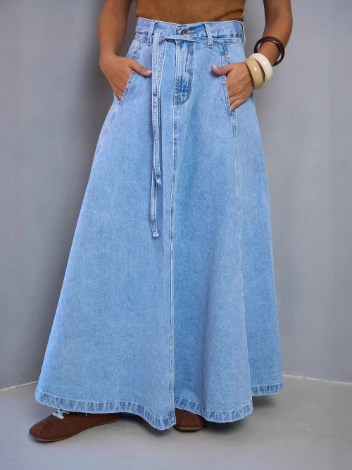 Person wearing a long denim skirt with a plain background