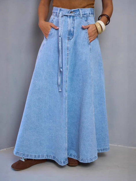 Person wearing a long denim skirt with a plain background