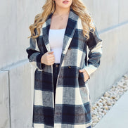 Woman wearing a plaid coat standing against a concrete wall.