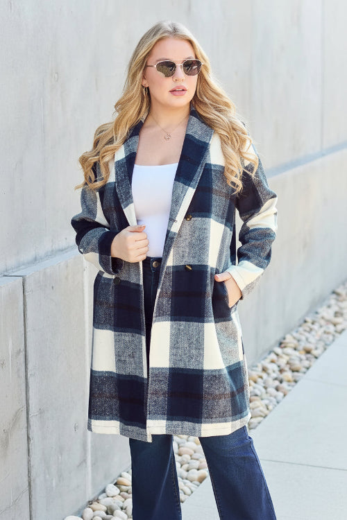 Woman wearing a plaid coat standing against a concrete wall.