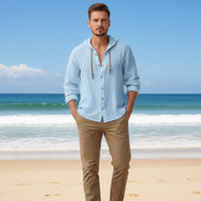 Man wearing a light blue button-up shirt with a beach in the background