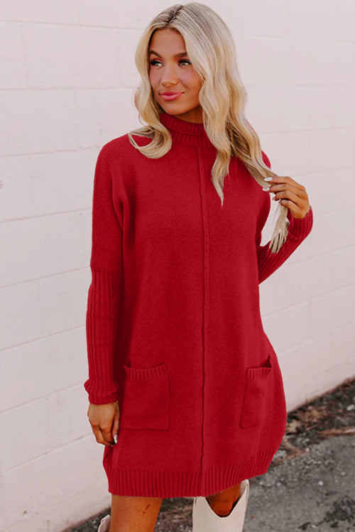 Woman wearing a red sweater dress against a white wall.
