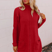 Woman wearing a red sweater dress against a white wall.