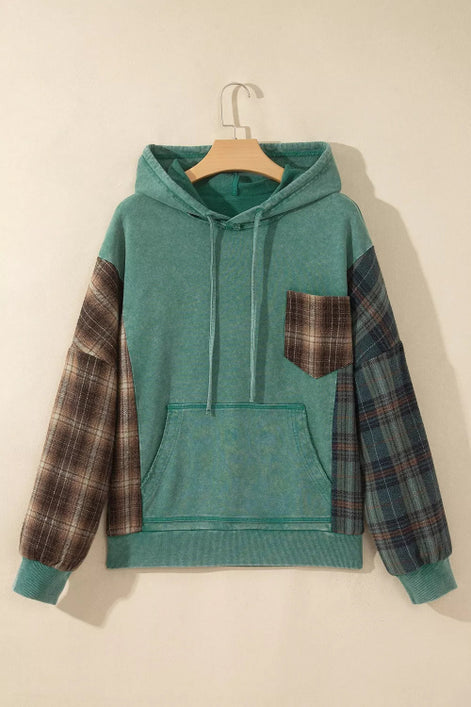 A teal green hooded sweatshirt hanging on a wooden hanger against a warm beige wall. The hoodie features solid teal green 
