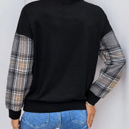 Person wearing a black sweater with plaid sleeves against a white background