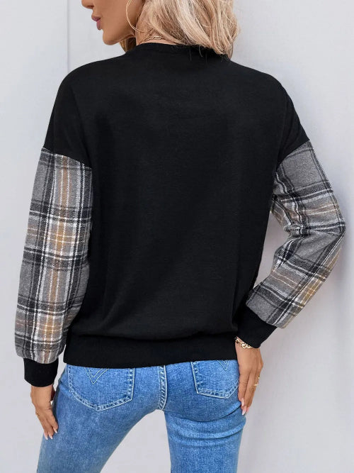Person wearing a black sweater with plaid sleeves against a white background