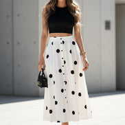 Woman sitting on a bench wearing a black top and white polka dot skirt.