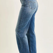 Angled back view of women’s Judy Blue straight-leg jeans showing rear patch pockets, faded blue denim, and stitched hems above brown slide sandals.
