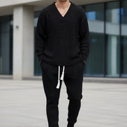 A person modeling a matching dark navy knit lounge set consisting of a long-sleeve V-neck sweater and jogger pants with a white drawstring, 
