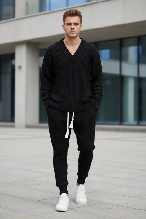 A person modeling a matching dark navy knit lounge set consisting of a long-sleeve V-neck sweater and jogger pants with a white drawstring, 