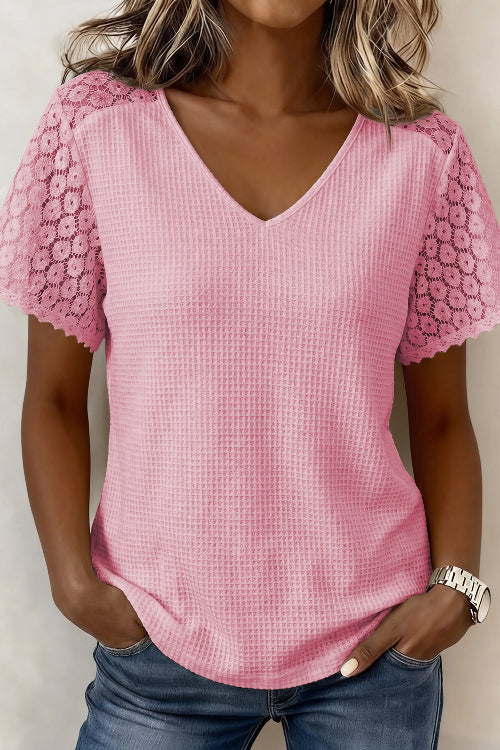 A woman wearing a pink waffle-knit short-sleeve top with floral lace shoulder panels and blue jeans, shown from the shoulders to the hips against a plain light background.