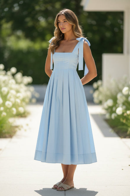 Woman wearing a light blue dress with a bow detail on a plain background