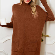 Woman wearing a brown sweater dress with a black hat against a white door background
