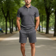 A man wearing a dark gray short-sleeve polo shirt and matching dark gray shorts with a textured diamond pattern,