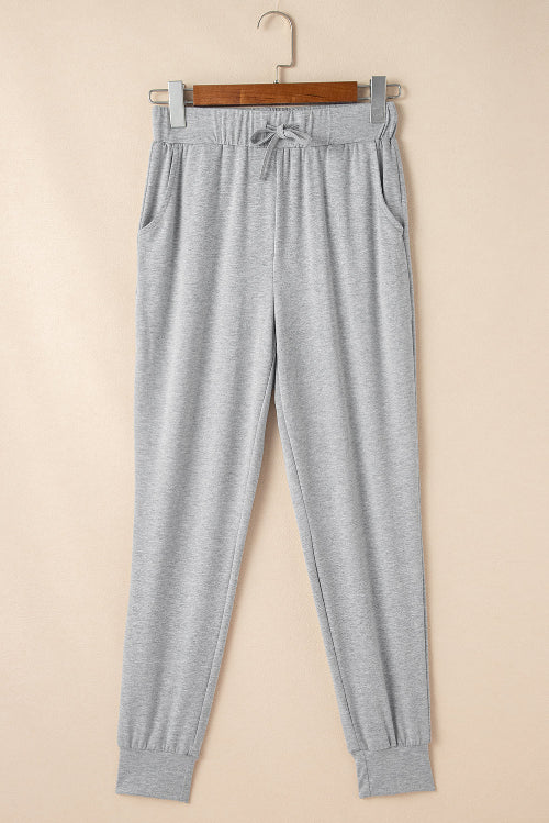 Gray sweatpants hanging on a wooden hanger against a beige background