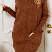 Woman wearing a brown sweater dress standing in front of a white door.