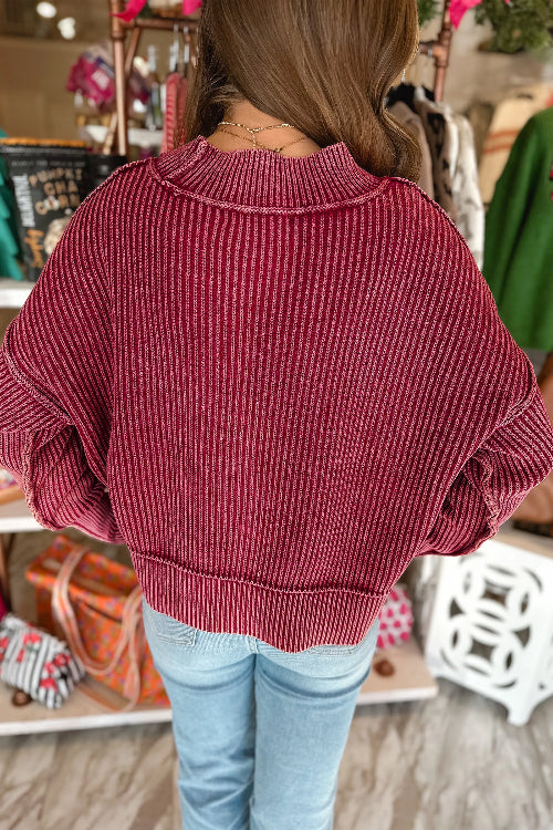 A woman viewed from behind wearing a ribbed knit sweater in a dusty rose or burgundy shade, paired with light blue 