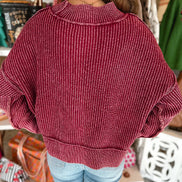 A woman viewed from behind wearing a ribbed knit sweater in a dusty rose or burgundy shade, paired with light blue 