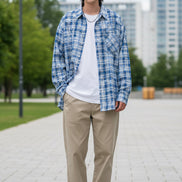Person wearing a blue and white plaid shirt with arms crossed on a white background