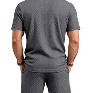 A man viewed from the back wearing a dark gray short-sleeve polo shirt and matching dark gray shorts, 