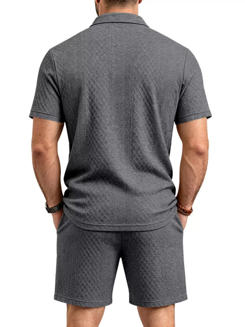 A man viewed from the back wearing a dark gray short-sleeve polo shirt and matching dark gray shorts, 