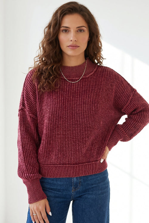 A woman wearing a ribbed knit crewneck sweater in a deep burgundy red, paired with blue jeans, 