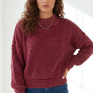 A woman wearing a ribbed knit crewneck sweater in a deep burgundy red, paired with blue jeans, 