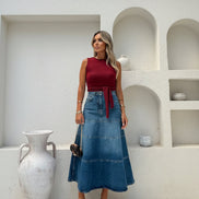Woman wearing a red top and blue denim skirt in a minimalistic setting.