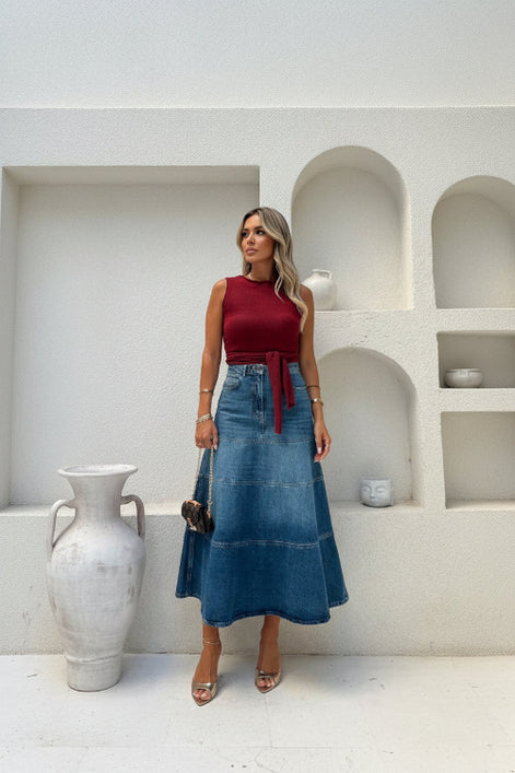 Woman wearing a red top and blue denim skirt in a minimalistic setting.