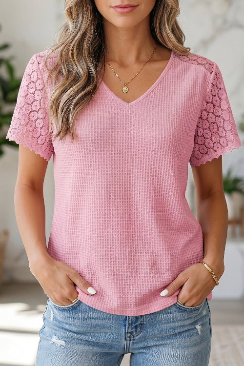 A woman wearing a pink waffle-knit short-sleeve V-neck top with floral lace flutter sleeves, paired with light blue jeans.