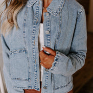 A woman wearing a light-wash blue denim jacket with scalloped edges over a white top and brown pants.
