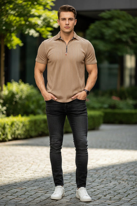Man wearing a brown polo shirt and black jeans standing outdoors with greenery in the background