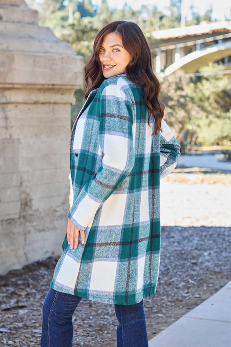 Woman wearing a plaid coat outdoors with trees and a building in the background