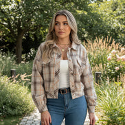 Person wearing a plaid shirt over a white top and blue jeans, holding a pen.