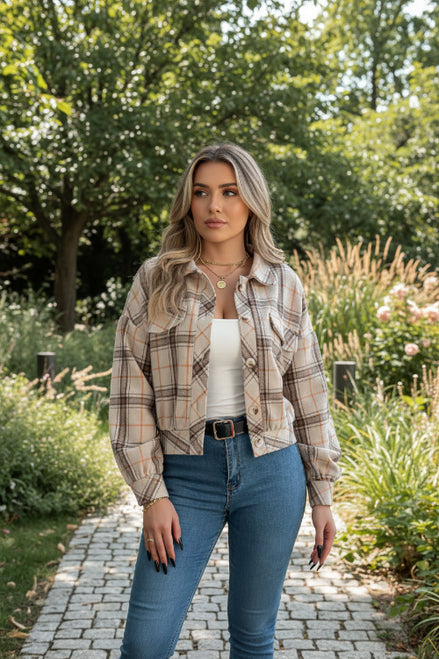 Person wearing a plaid shirt over a white top and blue jeans, holding a pen.