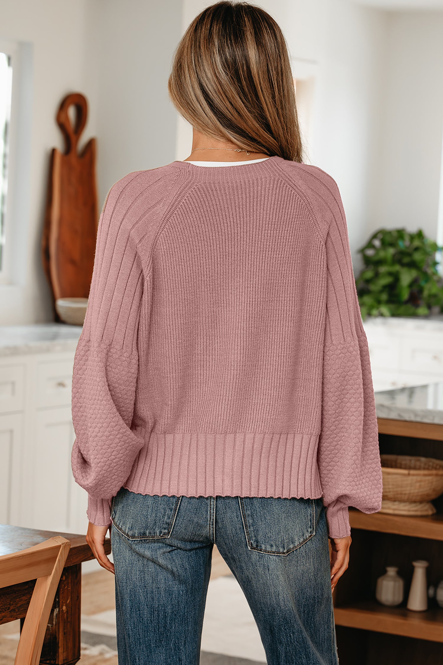 Person wearing a pink sweater and blue jeans in a kitchen setting