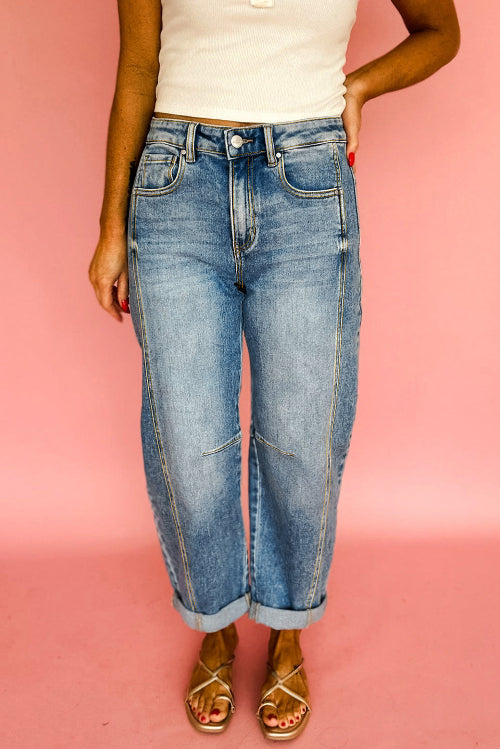 Person wearing blue jeans and a white top against a pink background
