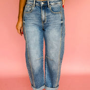 Person wearing blue jeans and a white top against a pink background