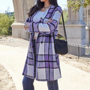 Woman wearing a purple plaid coat with a black handbag outdoors.